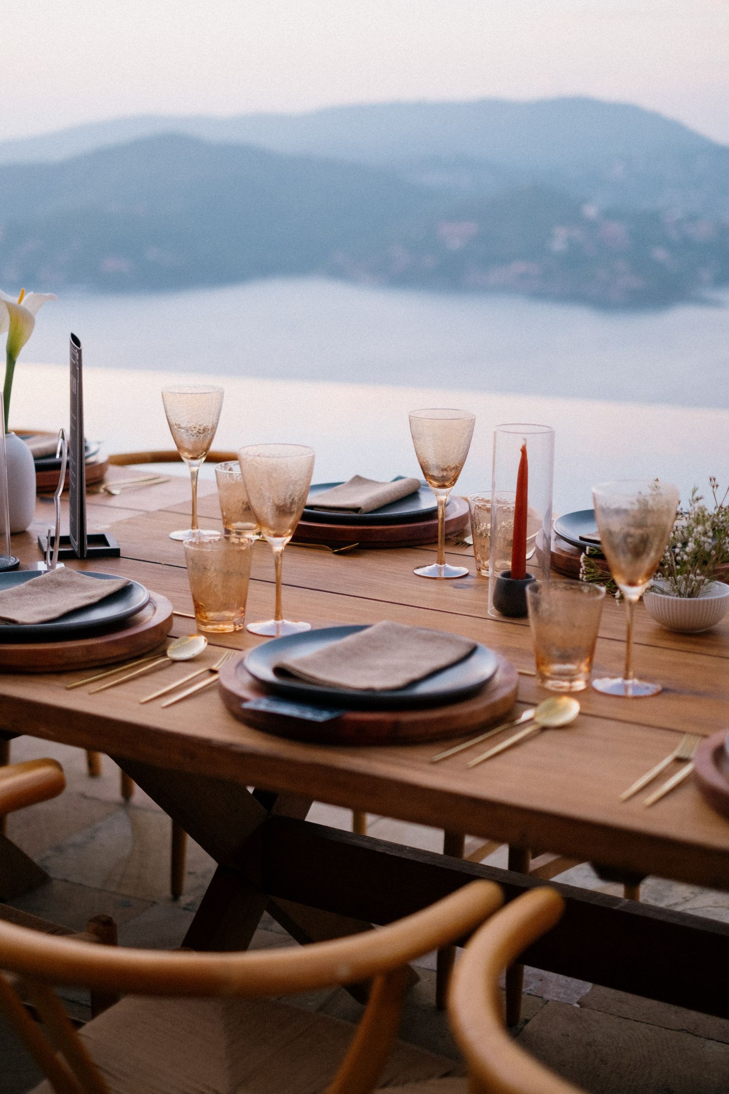 Elegant dinner table set with wine glasses and plates overlooking a misty mountain landscape at dusk.