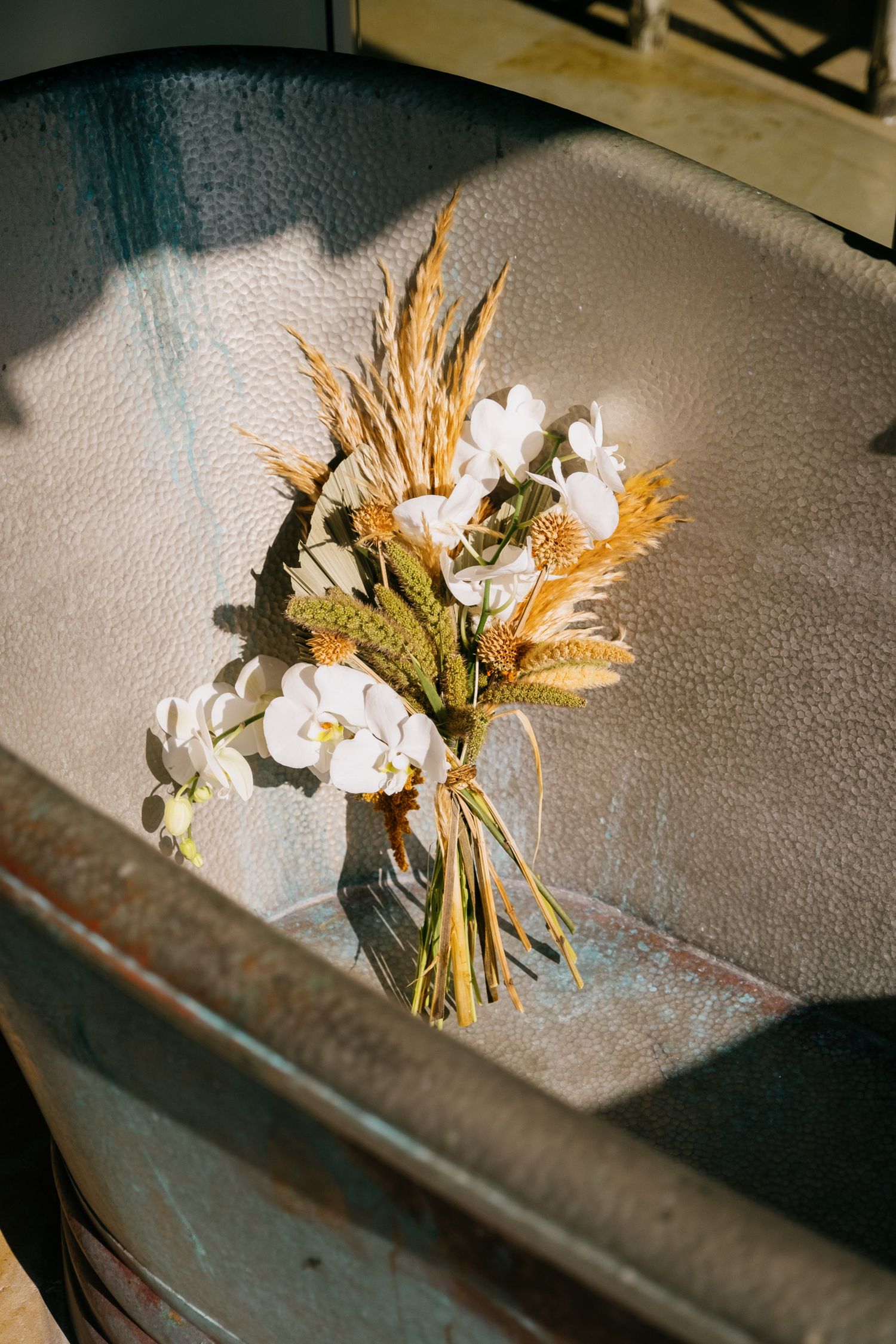 Rustic bouquet with white flowers and dried wheat stems in vintage metal container.