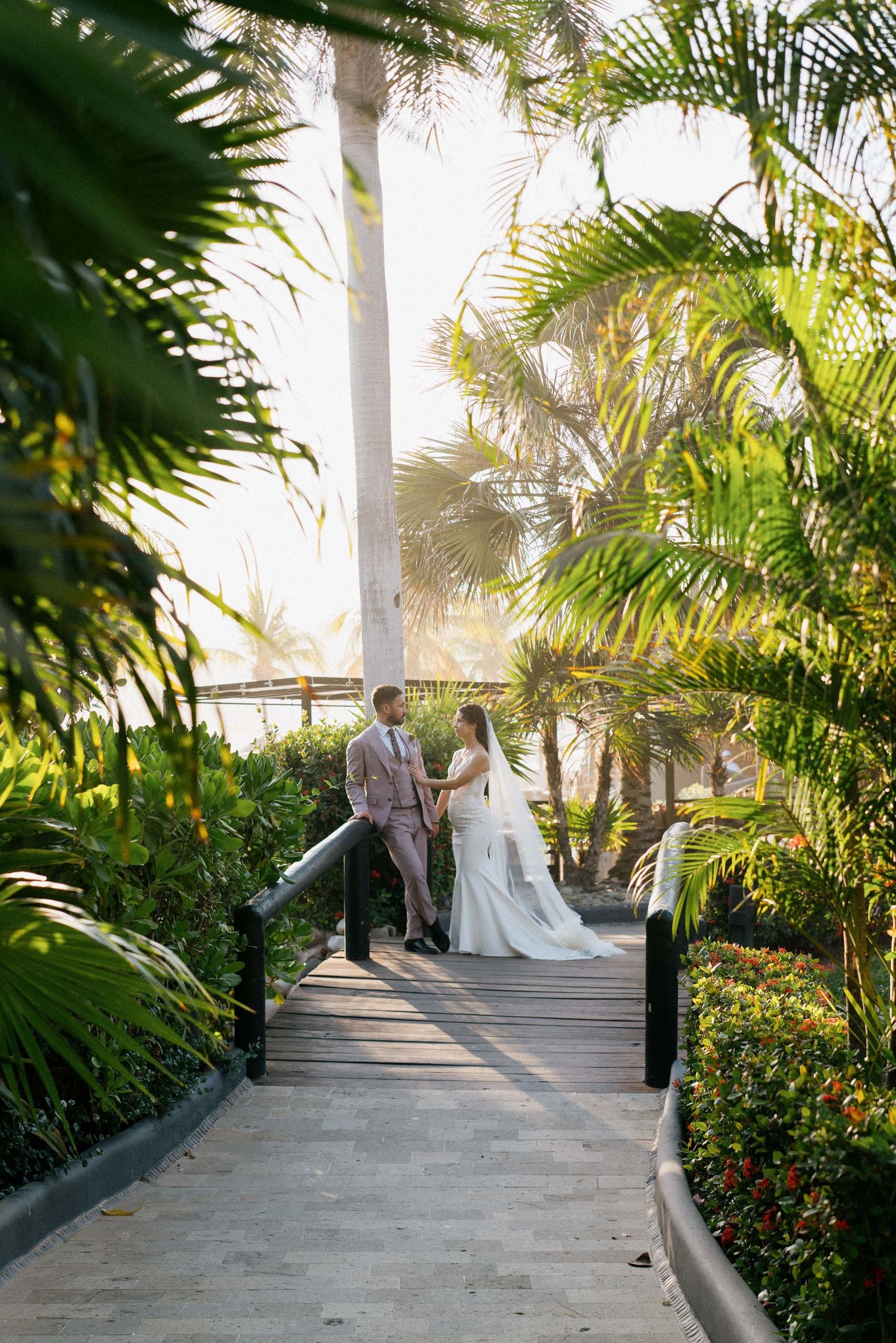 Couple poses on wooden walkway surrounded by lush tropical palm trees and gardens.