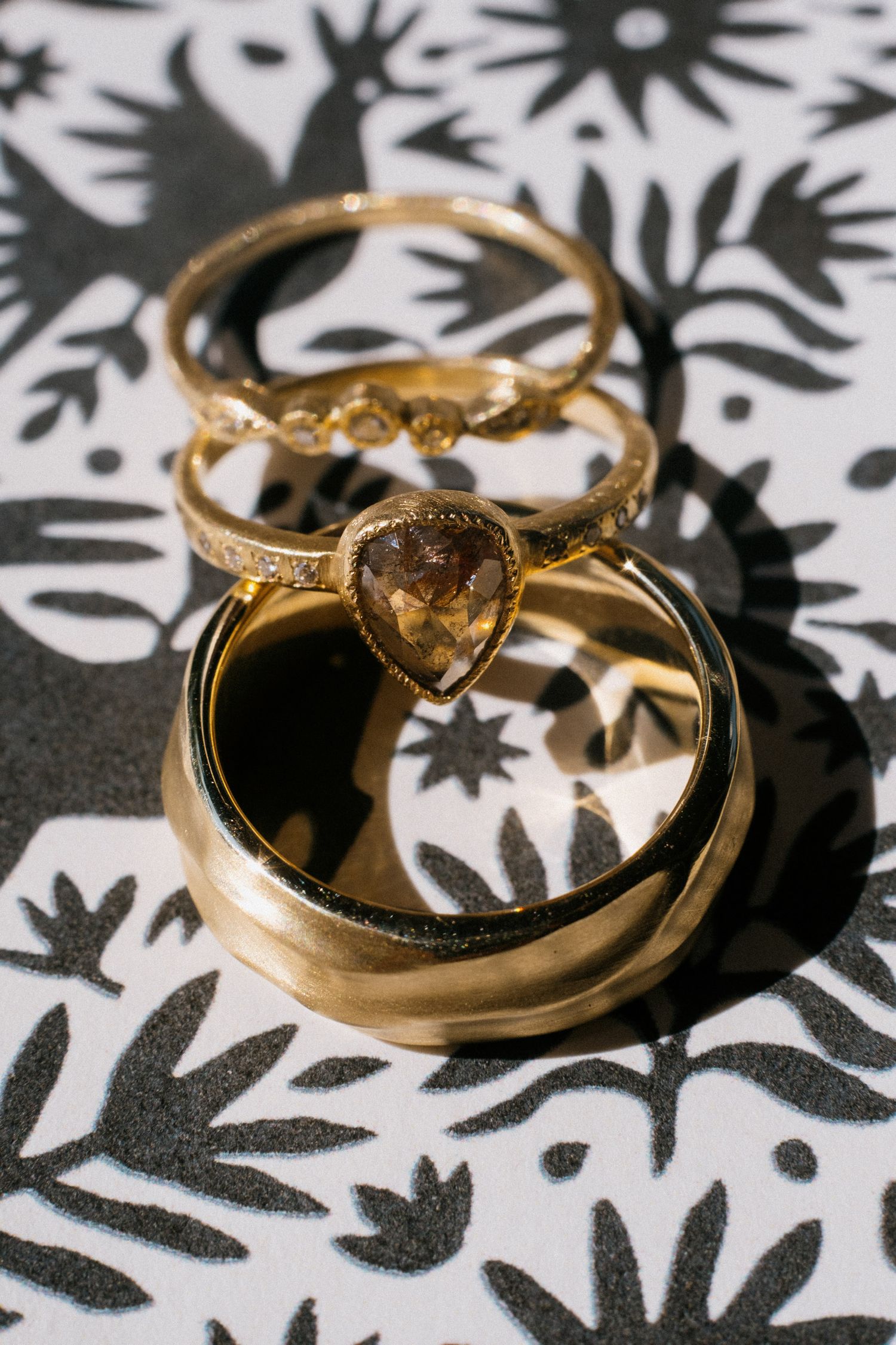 Gold wedding rings with gemstones photographed on a black and white floral patterned background.