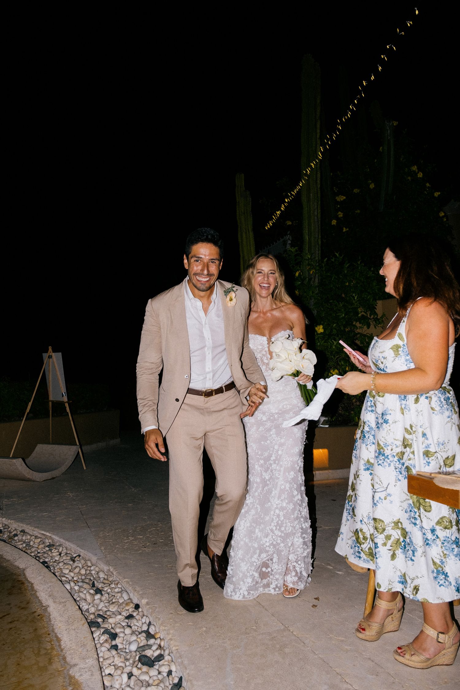 Wedding celebration at night with guests in formal attire under string lights.
