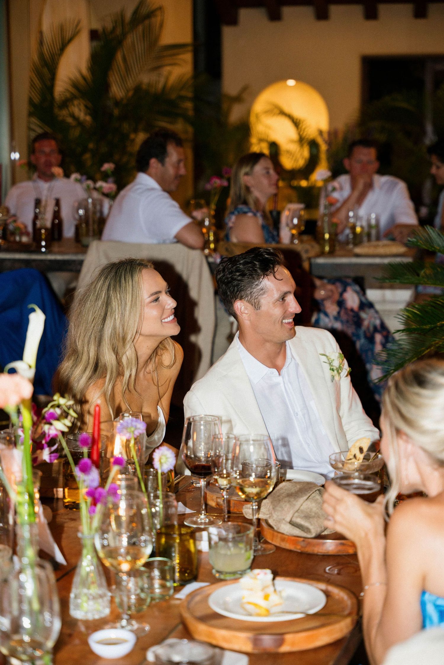 Wedding reception dinner table with candlelit ambiance and tropical decor at night.