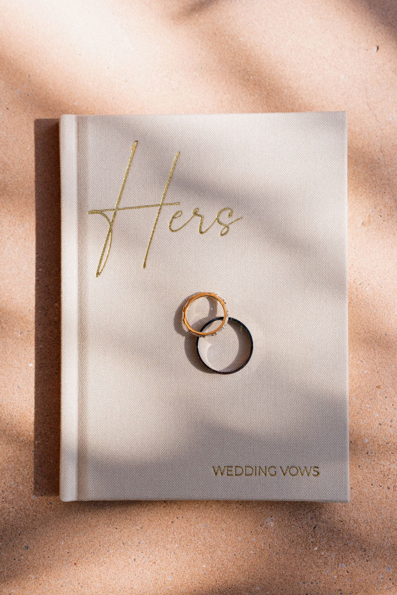 Wedding vows book with gold lettering and wedding rings casting soft shadows.