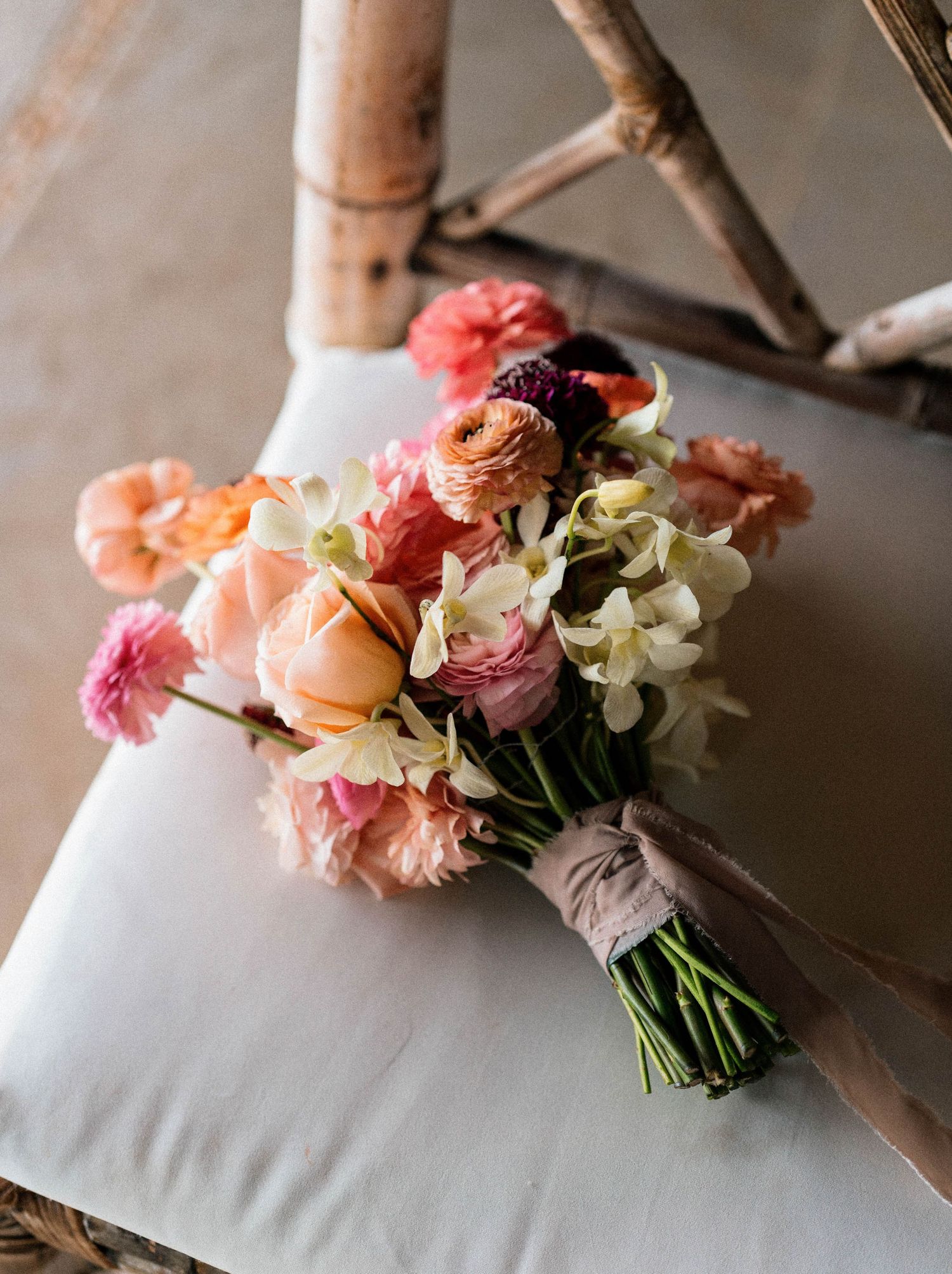 Romantic wedding bouquet with pink and peach flowers resting on white fabric.