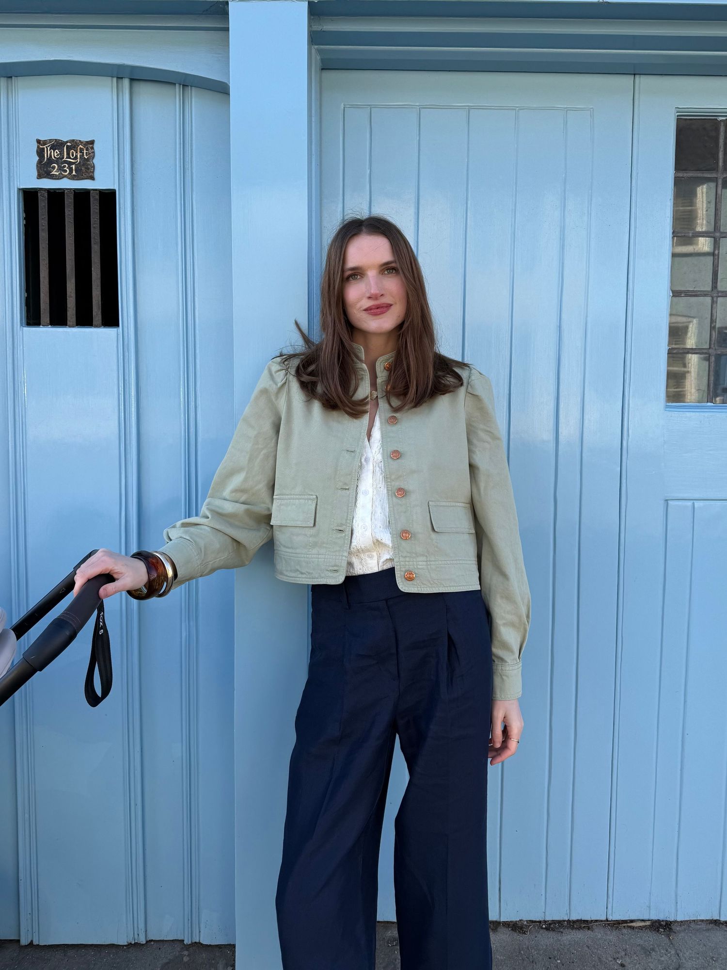 A series of fashion poses against a light blue wall wearing navy pants and a cropped beige jacket.