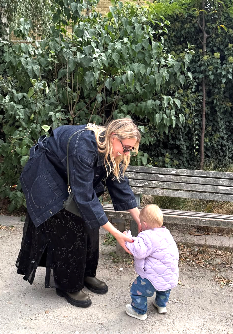 A tender moment between an adult and small child on a garden path near leafy green plants and a wooden bench.