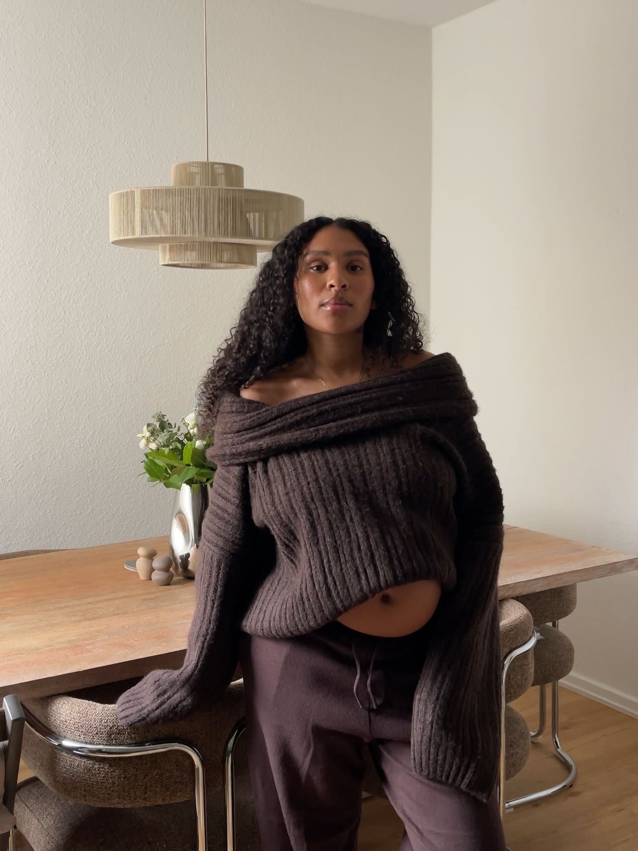 Woman in dark brown off-shoulder cable knit sweater and matching pants seated at a wooden dining table.