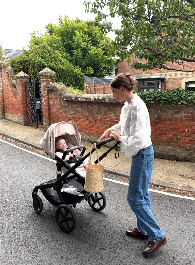 Person pushing a stroller with shopping bags along a brick wall lined residential street.
