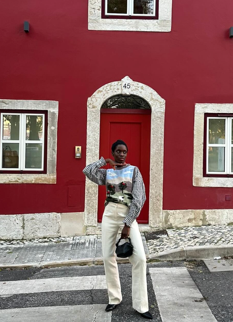 Stylish outfit against vibrant red building facade with ornate white trim and red door in urban setting.