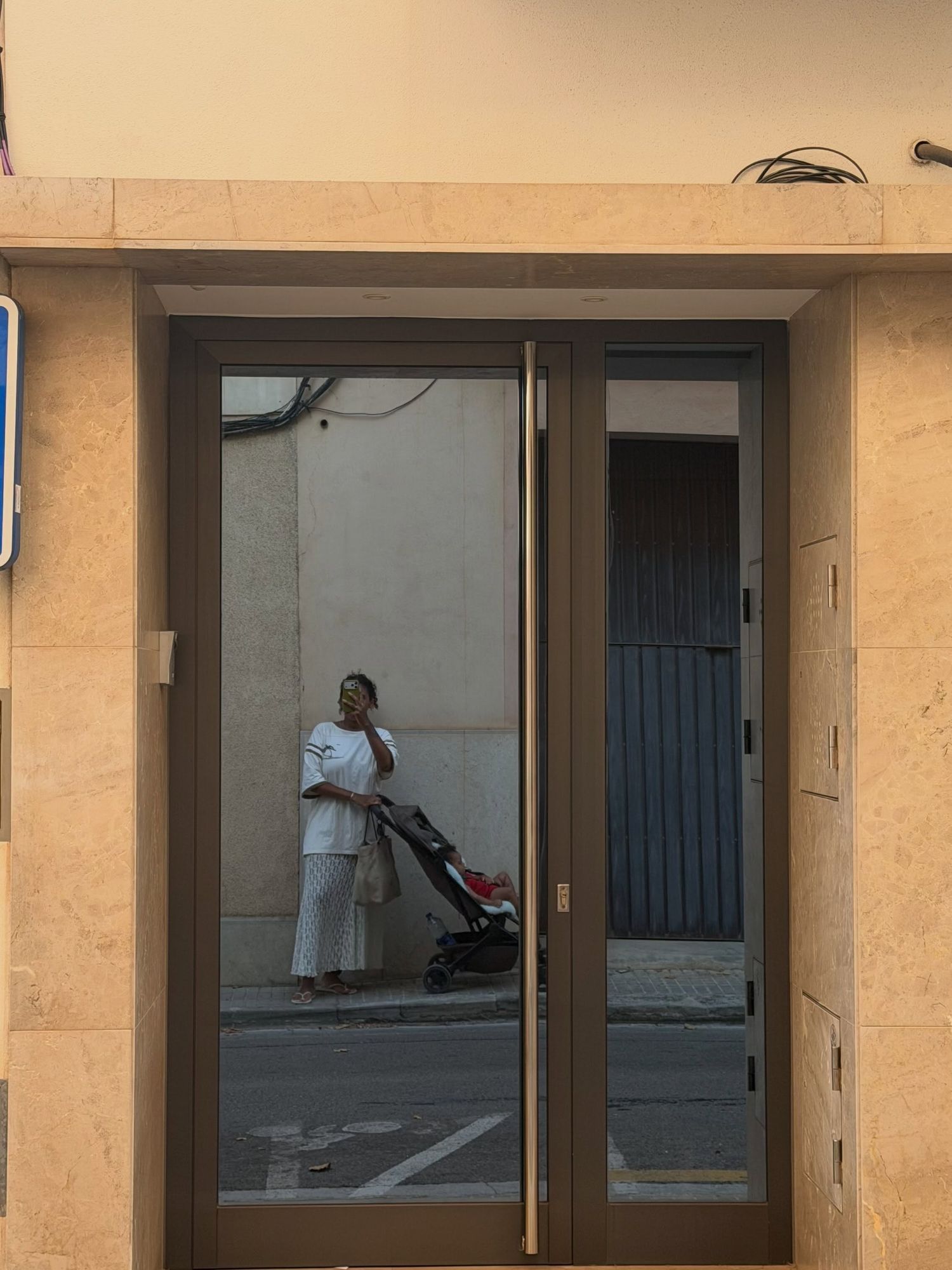 Woman with stroller reflected in glass door of modern building entrance.