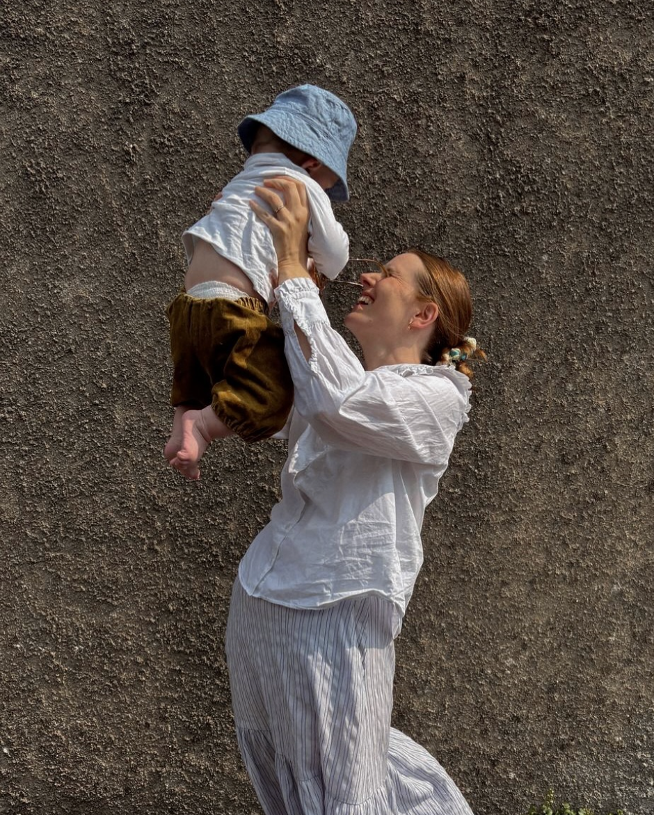 Two figures in white clothing dance and embrace against a textured grey wall in a sequence of intimate movements.