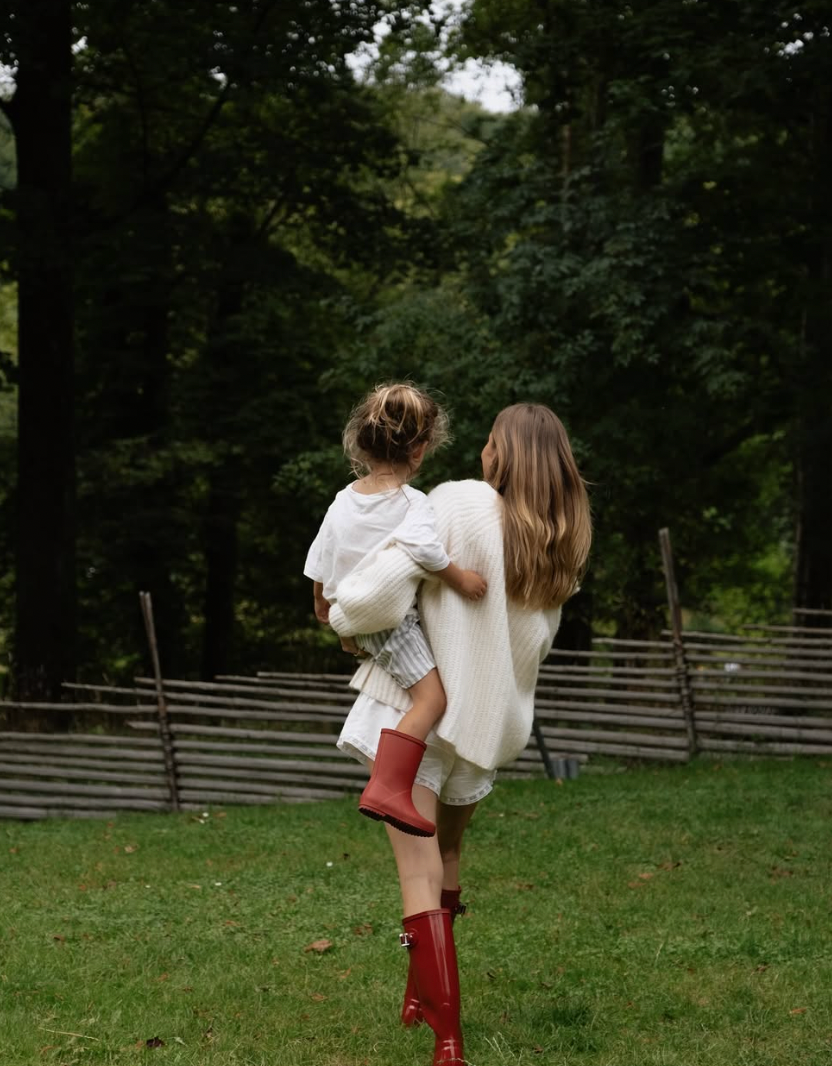 Two children play together in a grassy field near a wooden fence on a sunny day.
