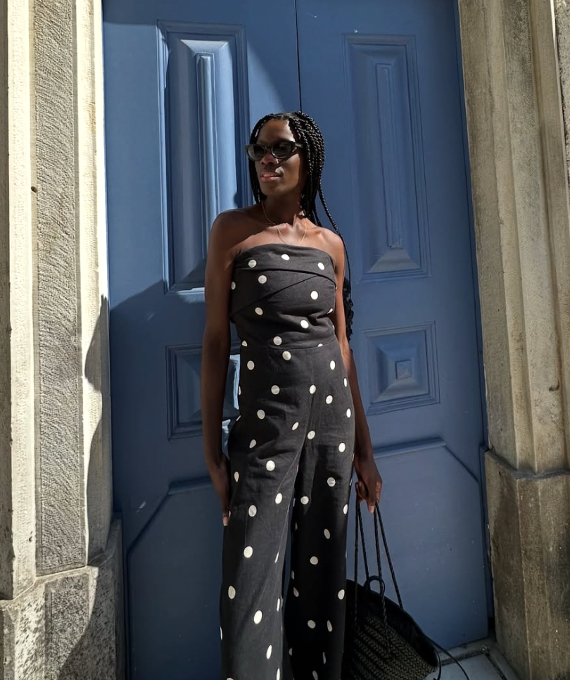 A woman in a black and white polka dot dress poses against a blue door and white columns.