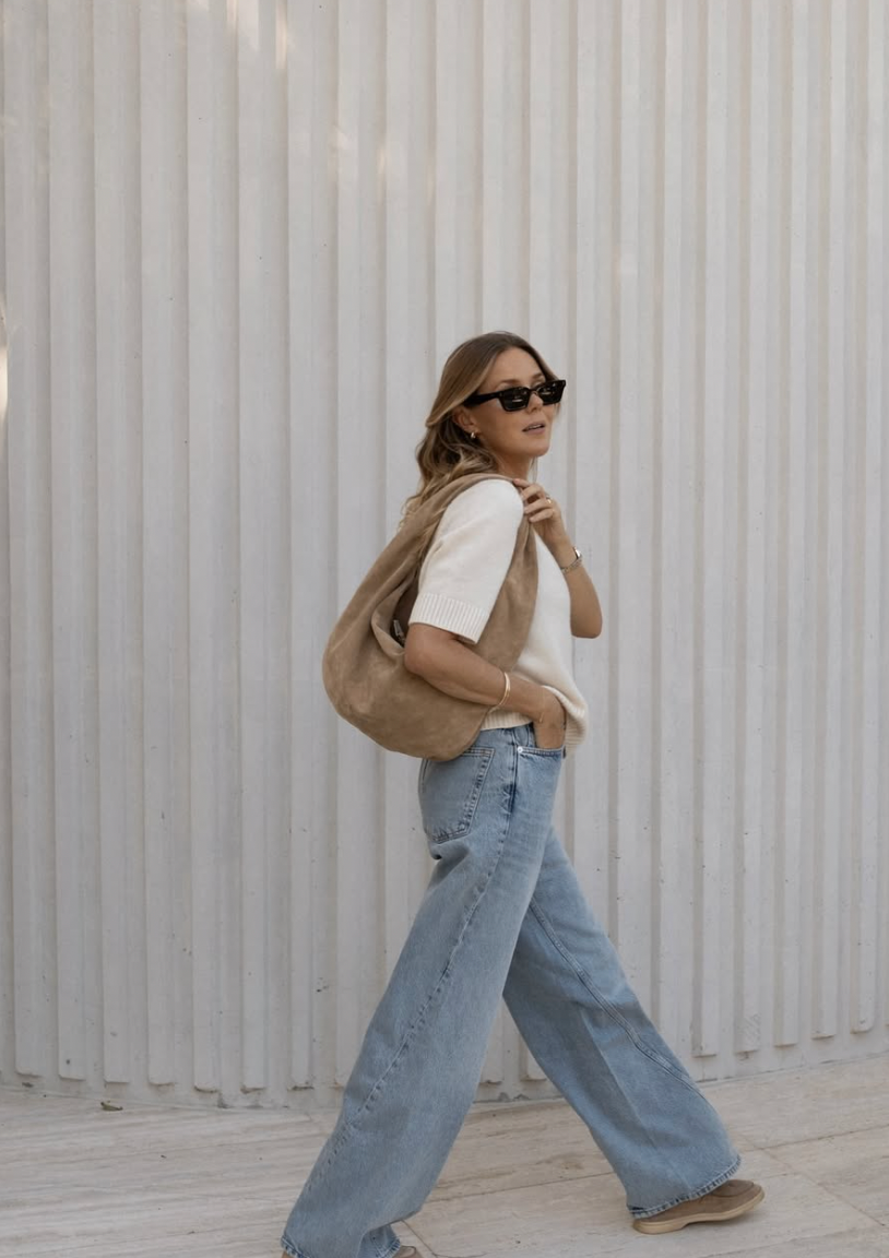 Person in sunglasses and light colored top with wide leg jeans poses against white corrugated wall in multiple shots.