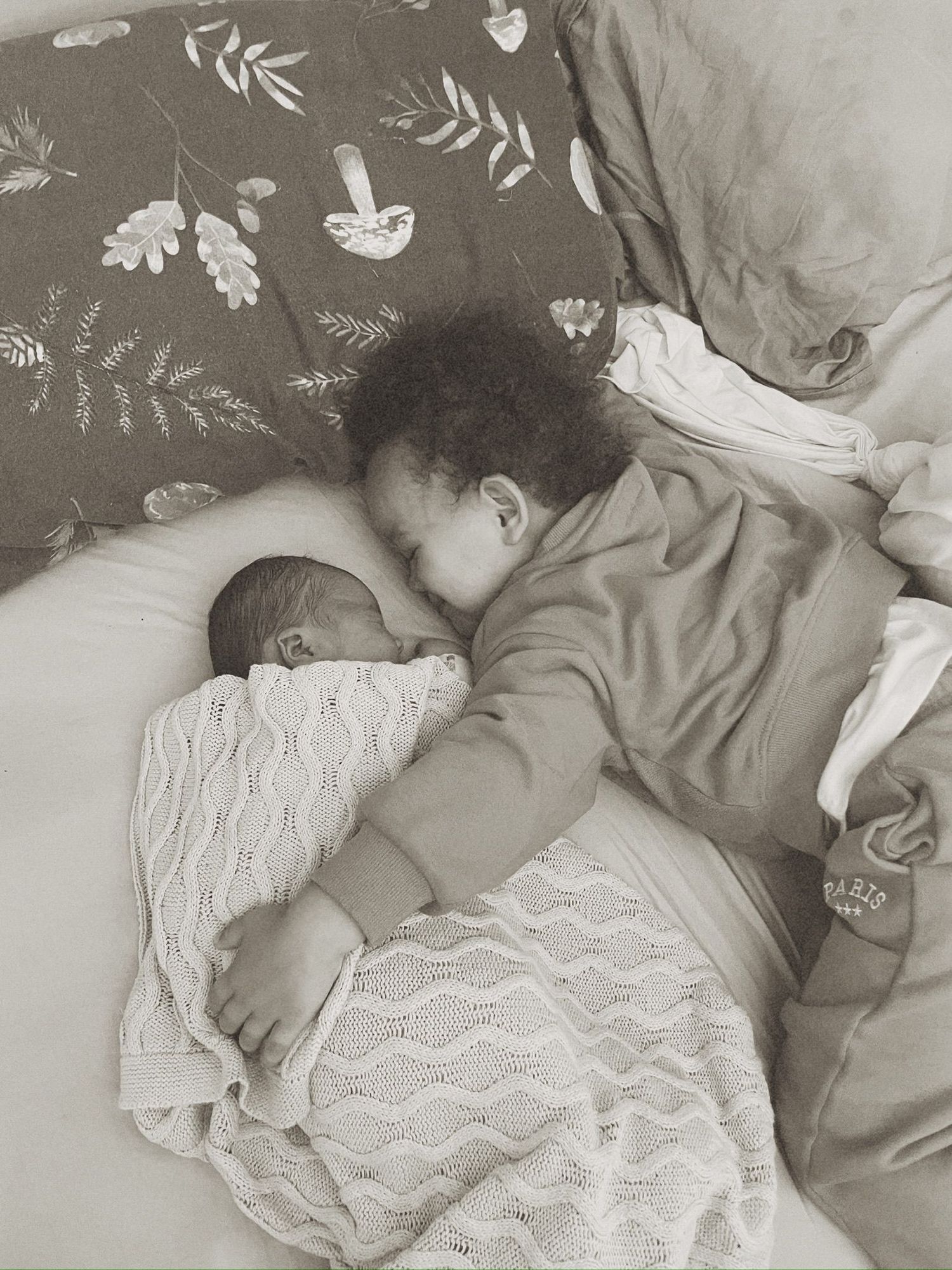 A sleeping baby lies on white lace bedding while wearing a gray onesie in a series of peaceful nap photos.