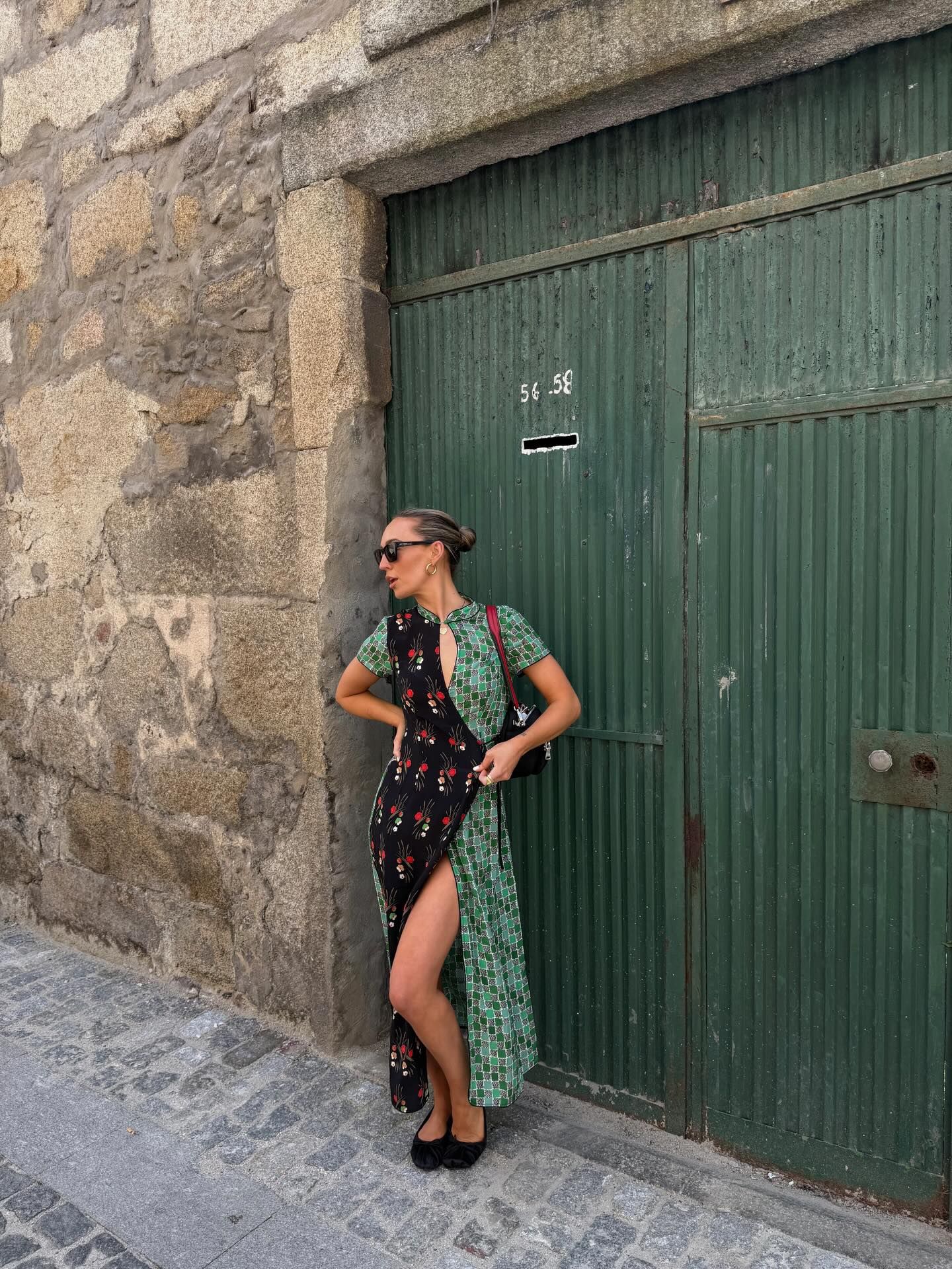Woman in floral green midi dress with slit posing against stone wall and green wooden door.