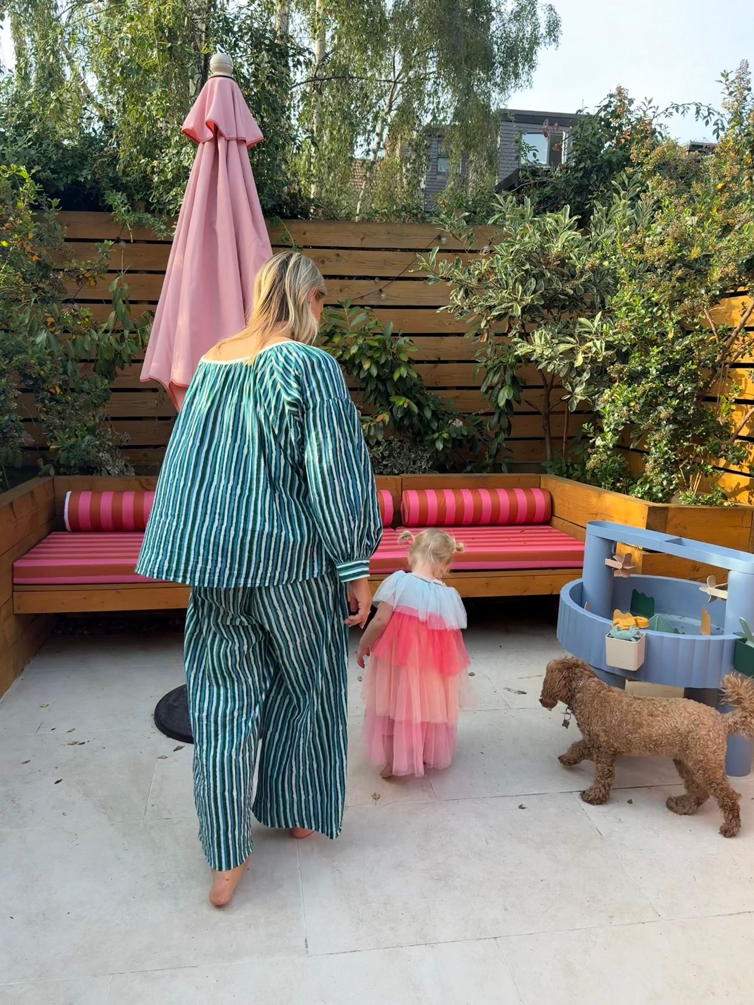 Woman in striped green outfit holds toddler girl in pink tutu dress in a stylish outdoor patio garden.