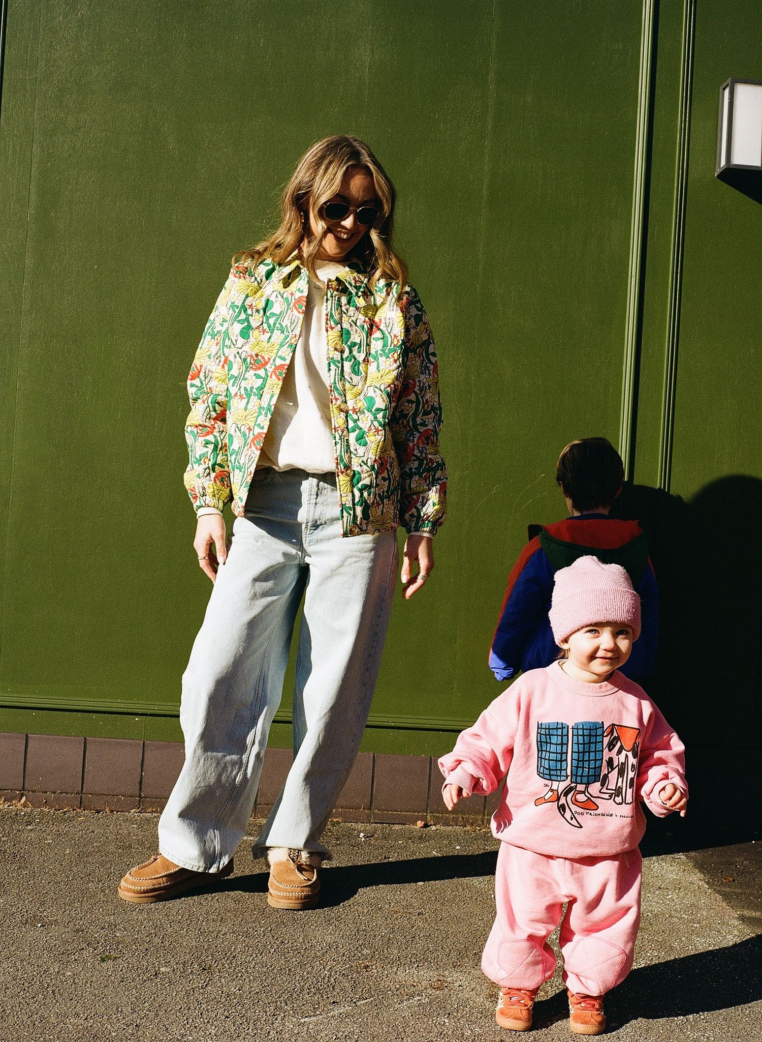 A sequence of photos showing a toddler in pink clothing learning to walk while holding onto a wall for support.