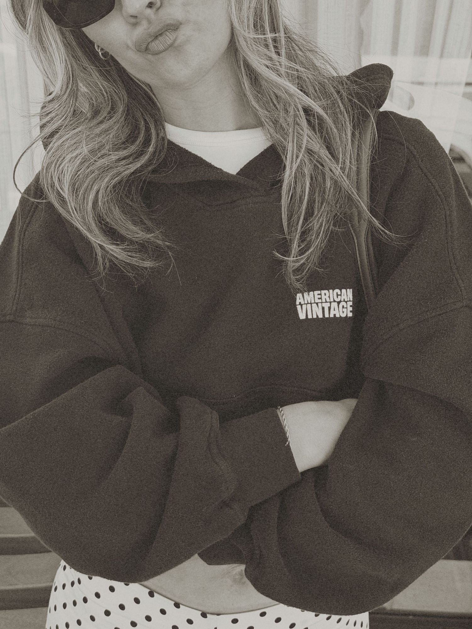 Woman in oversized American Vintage hoodie with crossed arms, black and white photo, polka dot skirt.