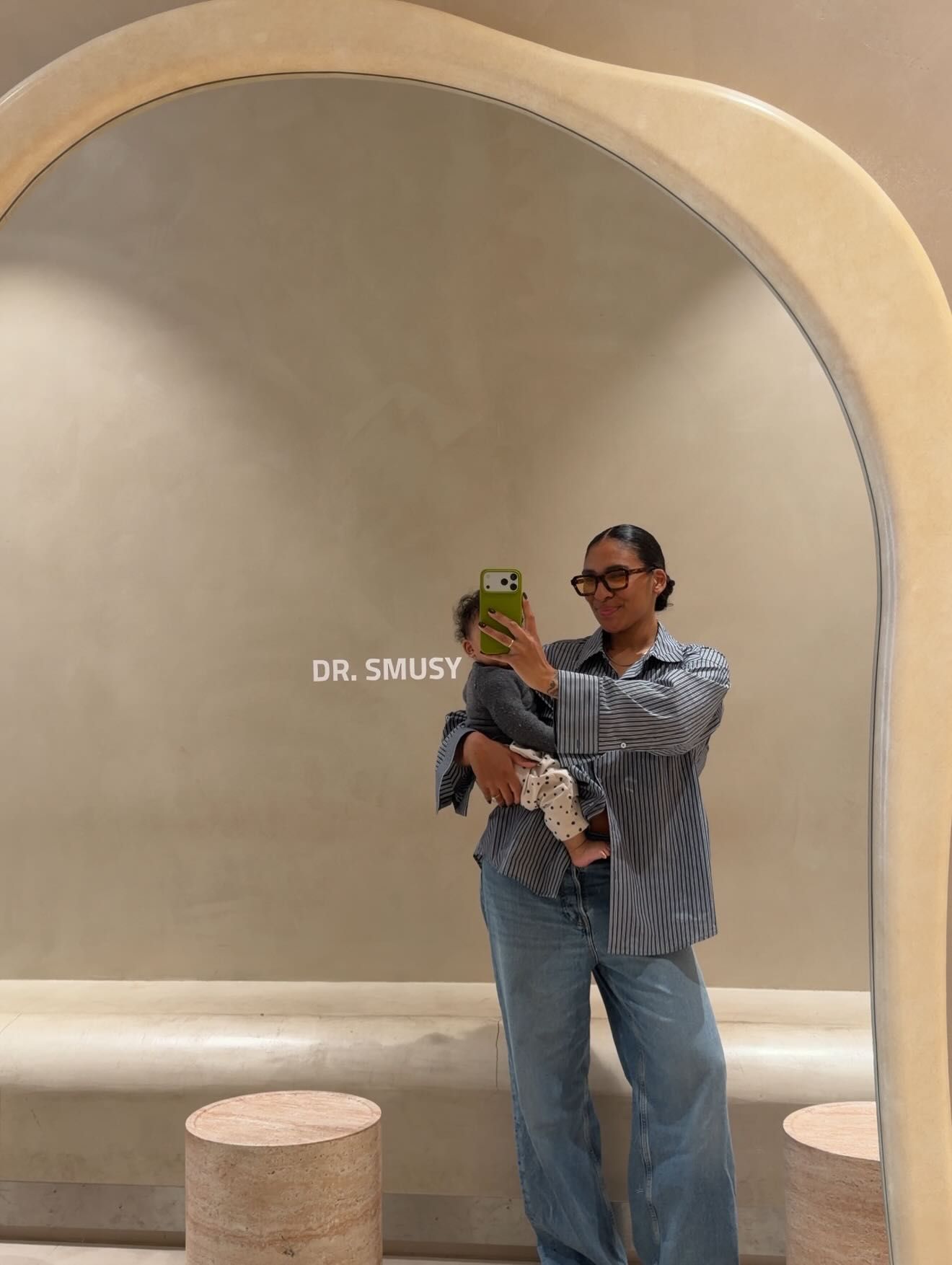 Woman in blue jeans and shirt takes mirror selfie at Dr. Smusy, holding green phone case.