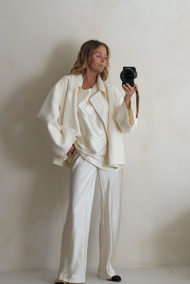 A model wearing a luxurious cream-colored oversized coat and trousers ensemble against a white wall.
