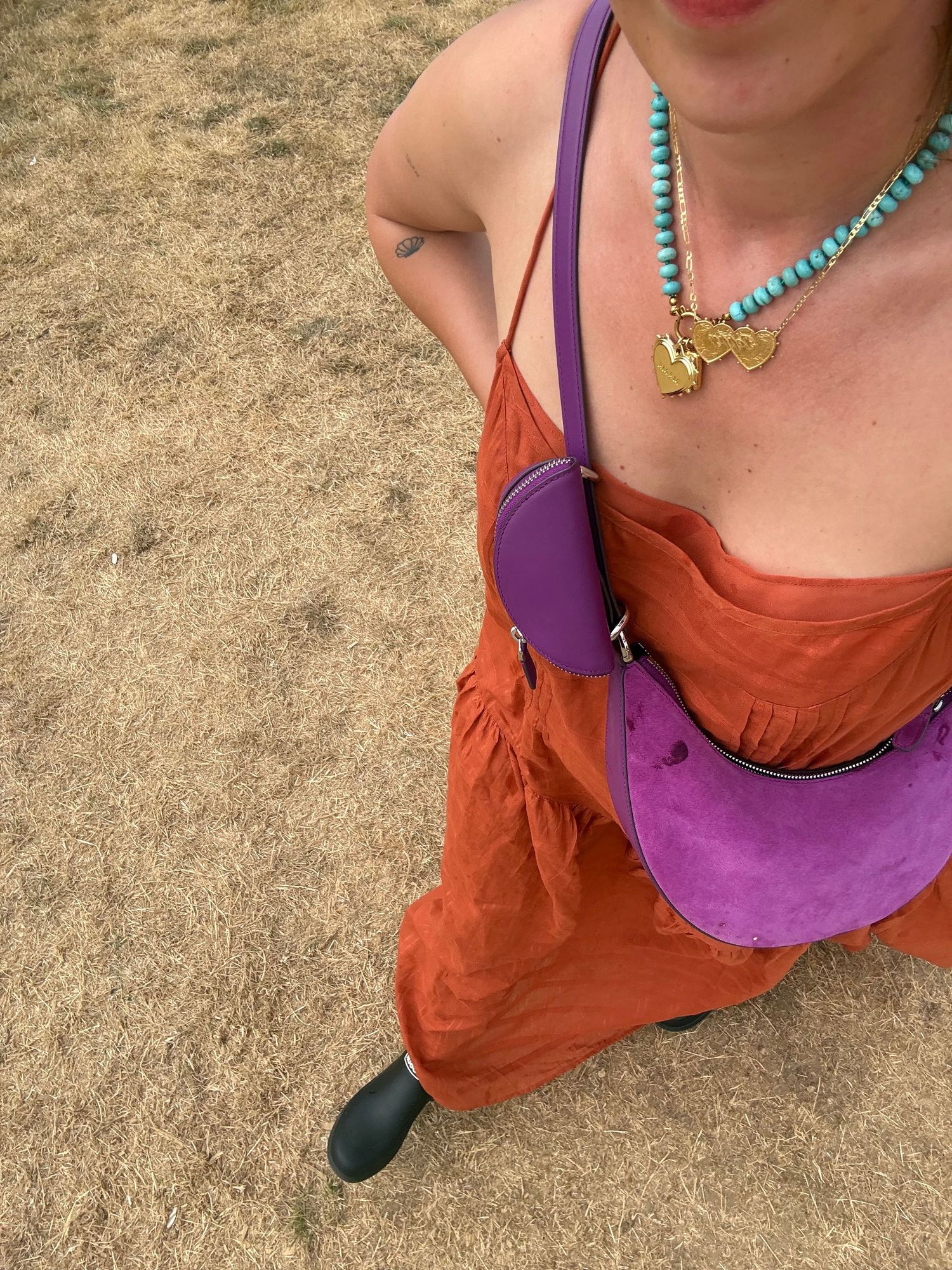 Woman in orange sundress with purple crossbody bag and turquoise beaded necklace standing outdoors on sandy ground.