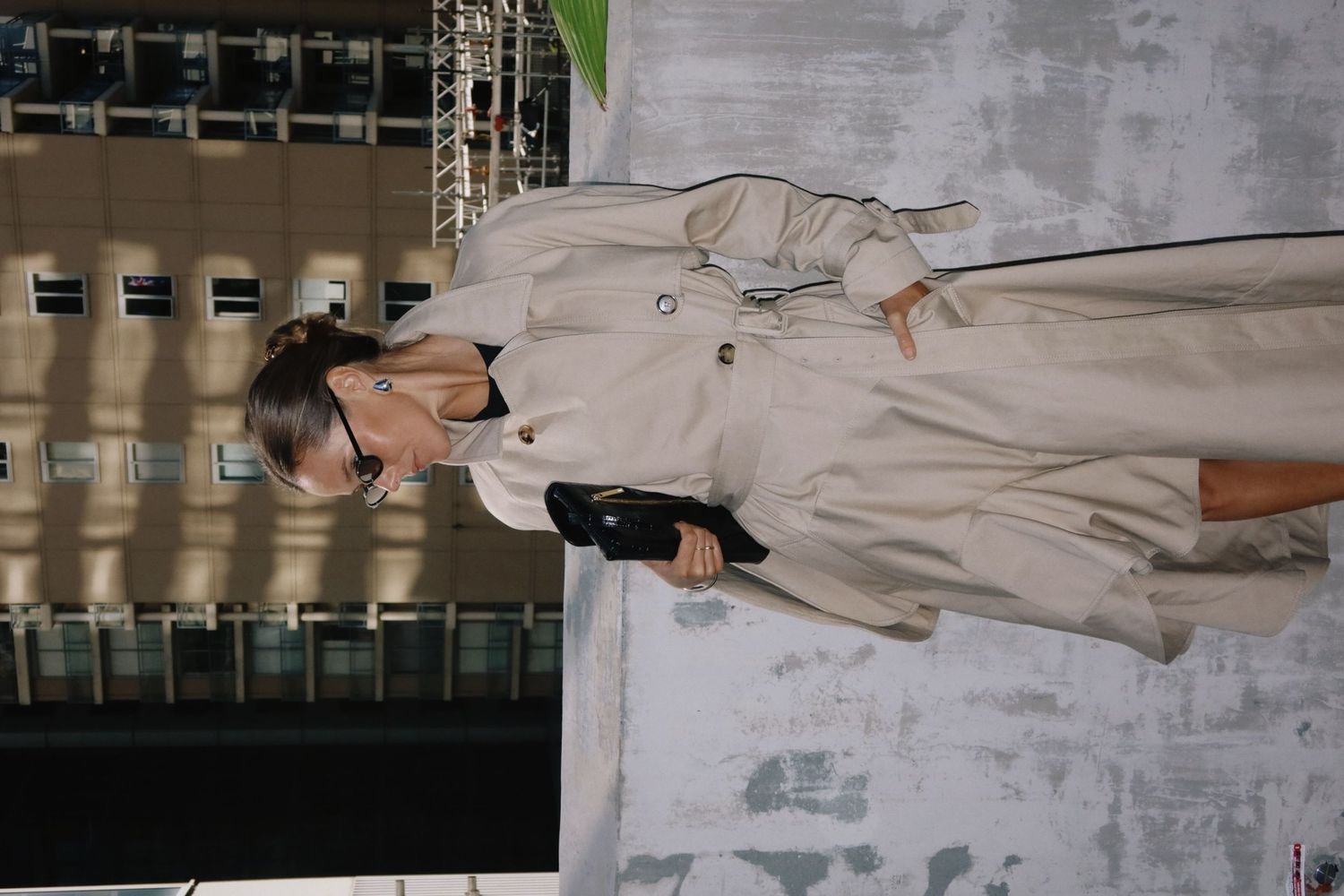 A model walks the runway wearing a stylish beige trench coat with sunglasses at a fashion show.
