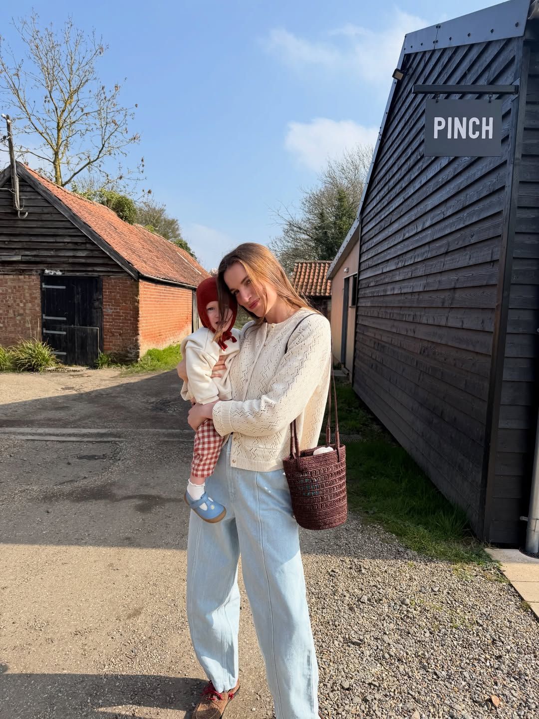 A series of photos showing someone in a cream sweater and jeans posing against a black wooden building exterior.