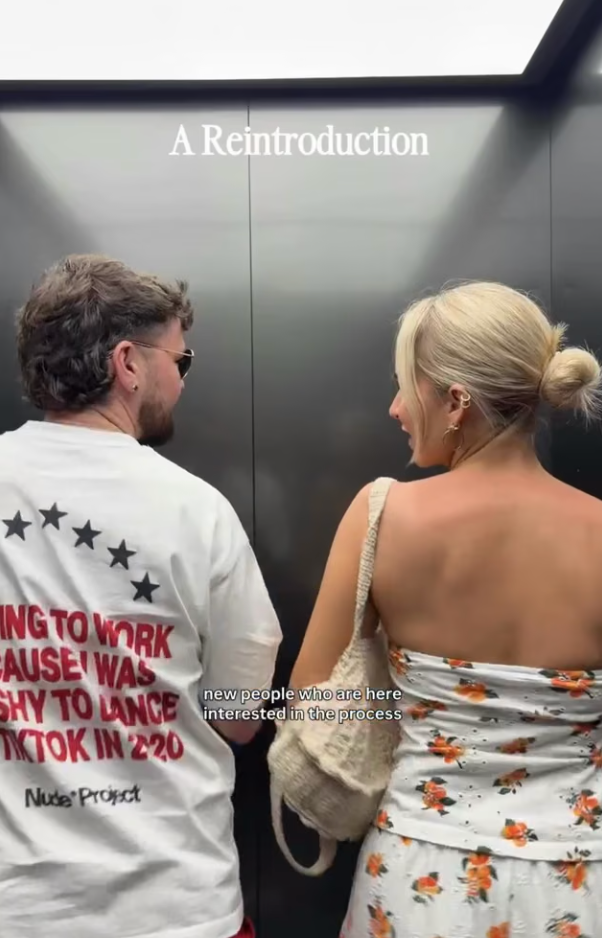 Couple standing in elevator, man in white graphic tee, woman in floral dress, text overlay reads A Reintroduction.