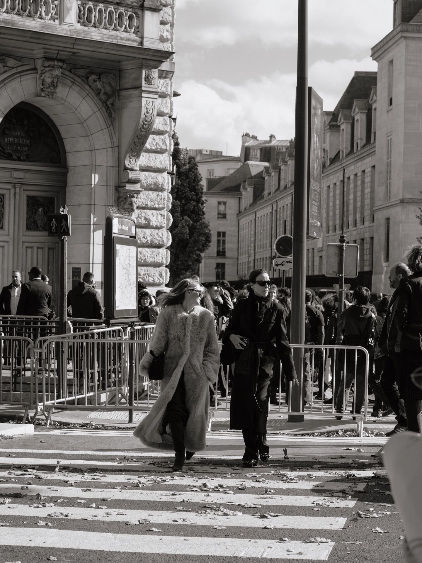 Black and white street photo of elegantly dressed pedestrians crossing a zebra crossing near a grand Parisian building.