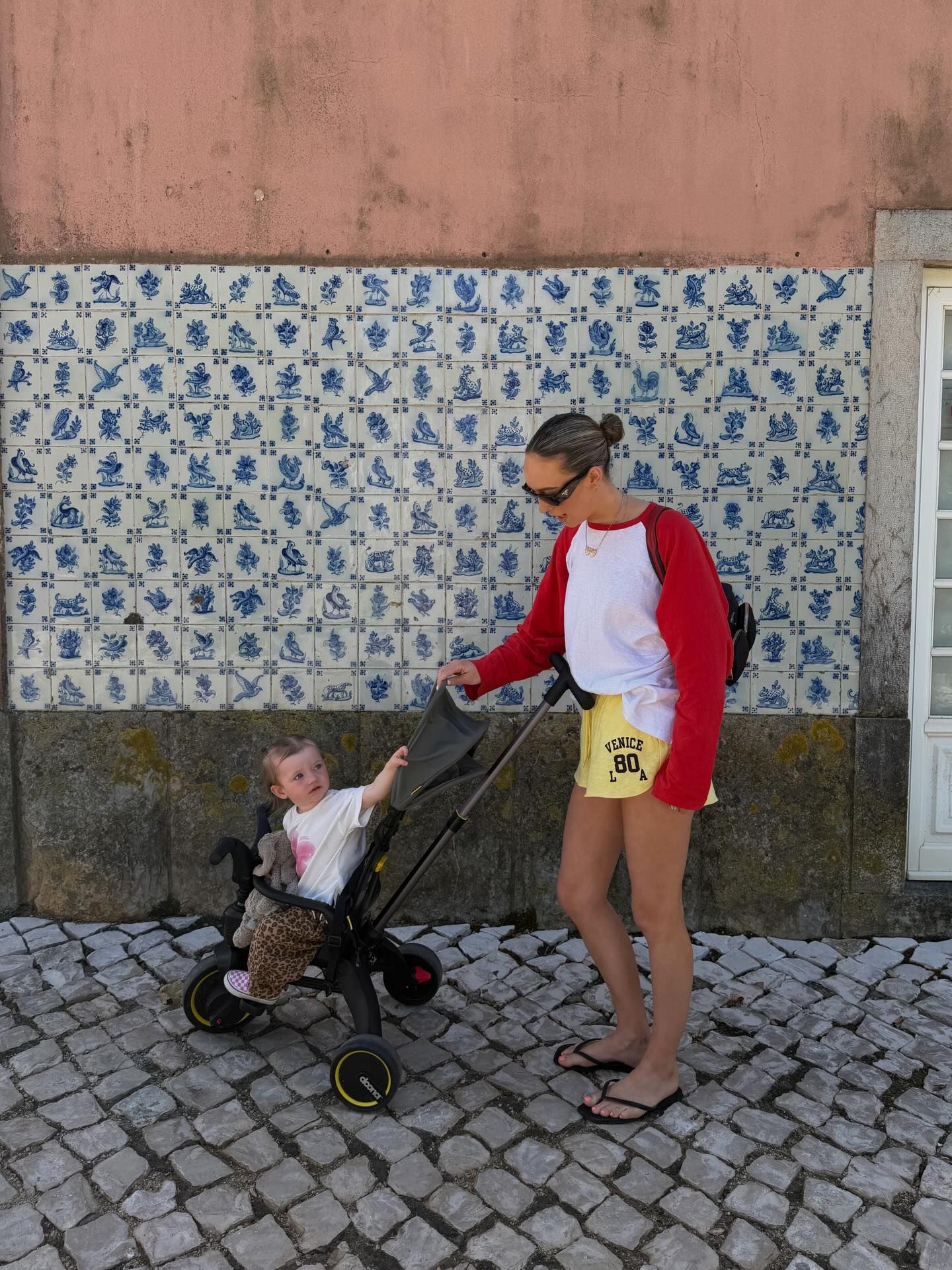 Woman pushing a baby stroller past blue and white Portuguese azulejo tiles on a cobblestone street.