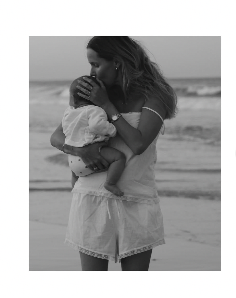 A couple embraces tenderly on a sandy beach in black and white.