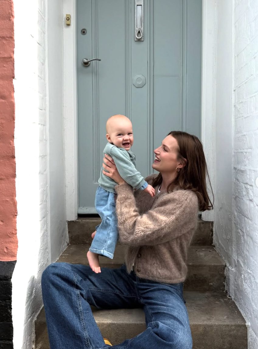 A parent and baby share a joyful moment playing together on concrete steps outside a blue door.