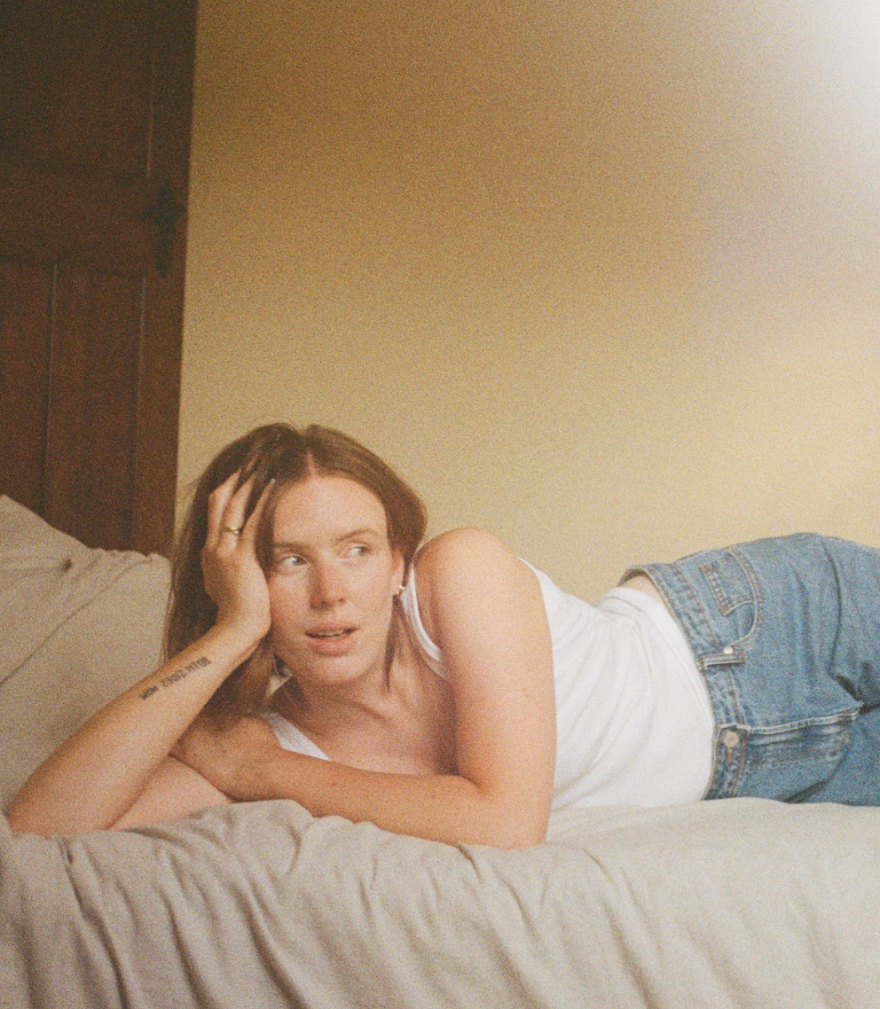 Person lying on white bedding wearing jeans in a dreamy boudoir style photoshoot.