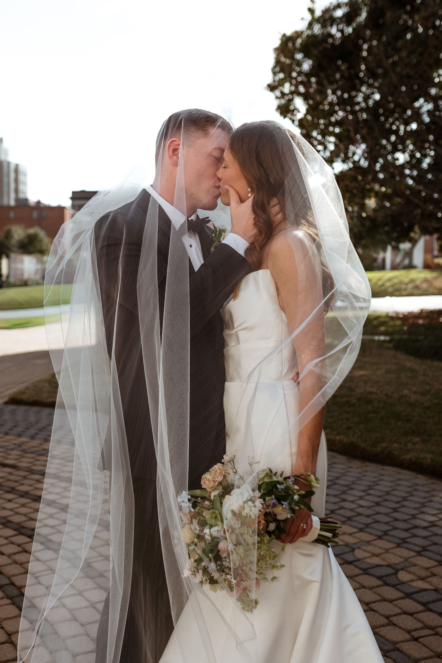 Bride and groom kissing under the bride's veil on their wedding day.