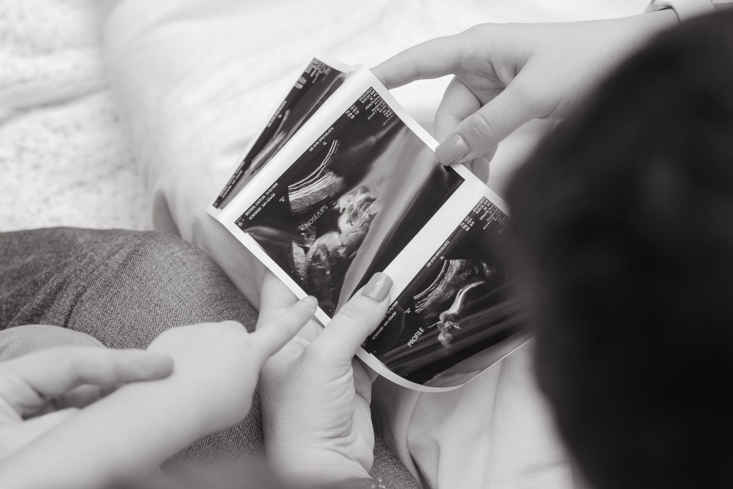 A mom and dad with the son looking at an ultrasound photo. The son is pointing at the photo. Black and white image.