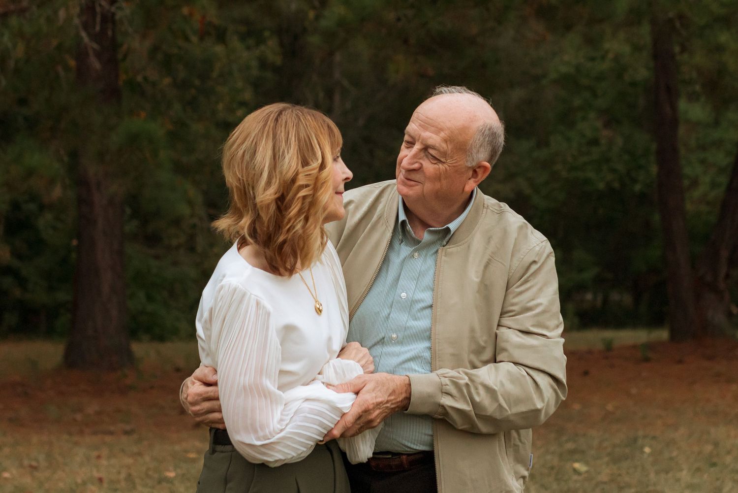 Senior couple in a field hugging and holding hands looking at each other and smiling in love.