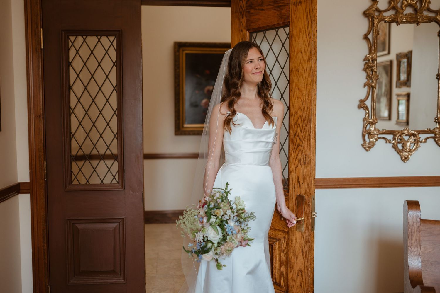 Bride holding bouquet while looking off in the distance, leaning on a door.