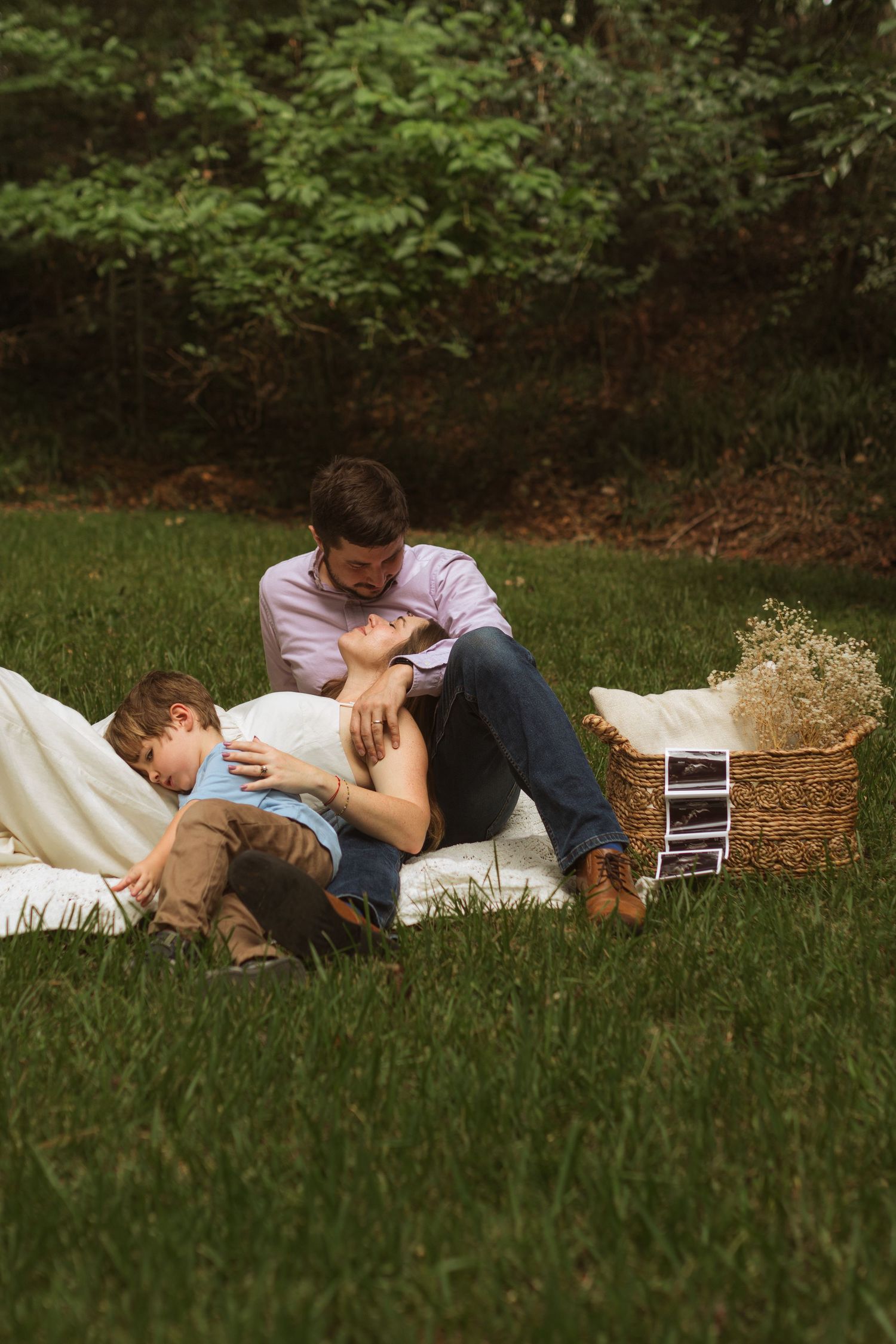 A family laying on the ground together with a basket that has ultrasound photos and flowers in it.
