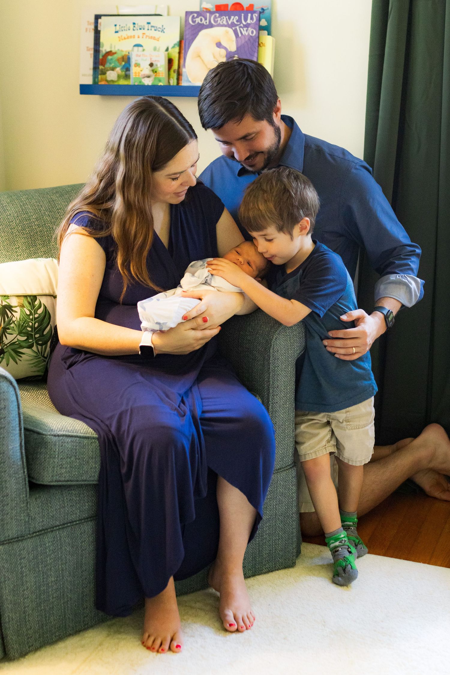 A lovely family of four including gathered together in a nursery. A mom, dad, and four year old son are all looking at a newborn baby.
