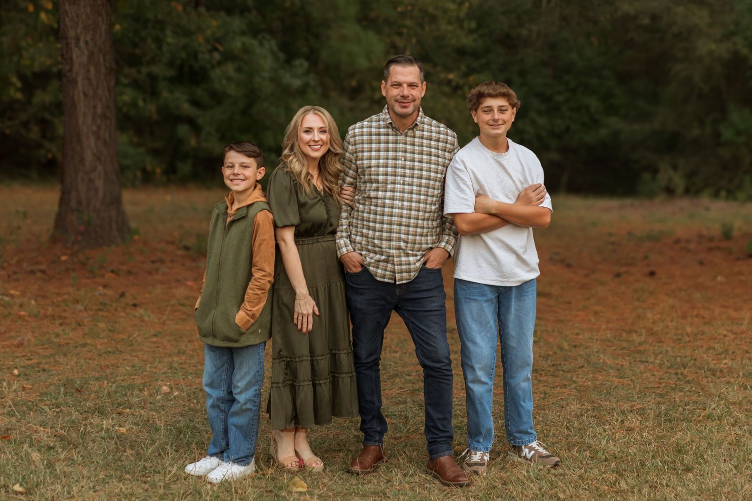 A beautiful family of four in a field. A mom and dad with a 10 year old son and 16 year old son posing for a family portrait.