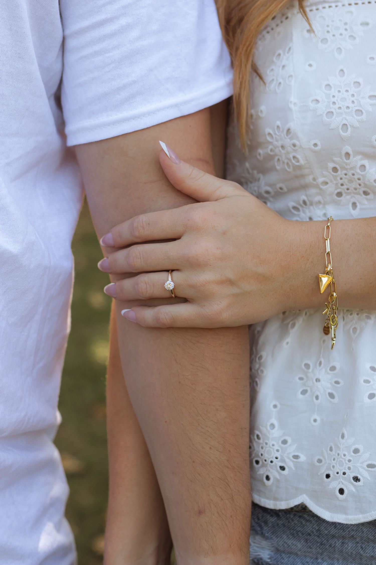 A close up on an engaged couple. The woman is leaning beside the man with her hand resting on his arm, ring showing.
