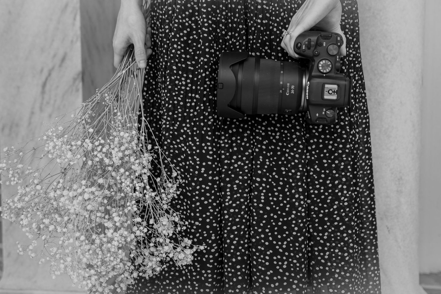 Photographer in a skirt holding a camera and baby's breath flowers.