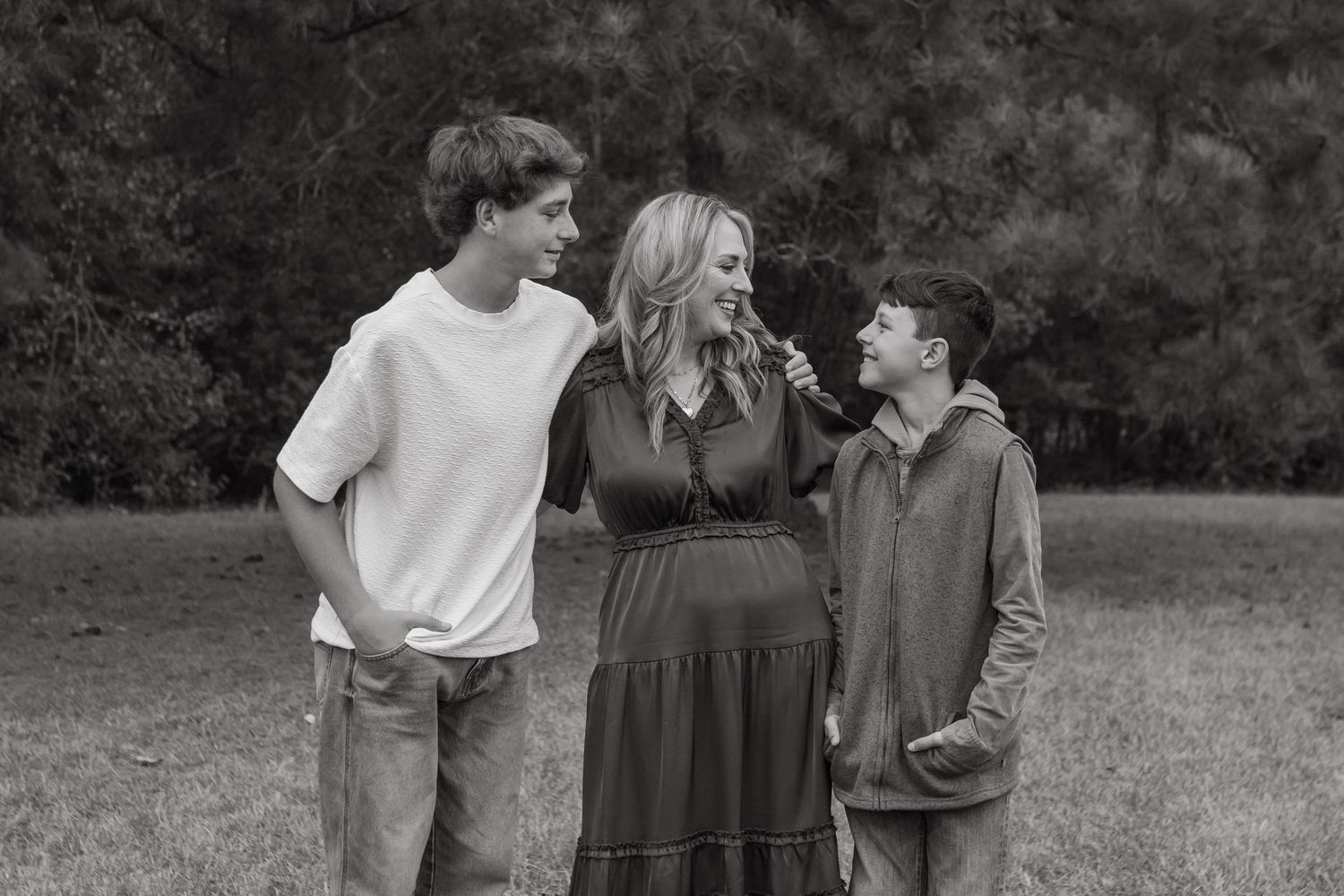 A mom in a field with her arm wrapped around her two sons. Everyone is smiling at each other.