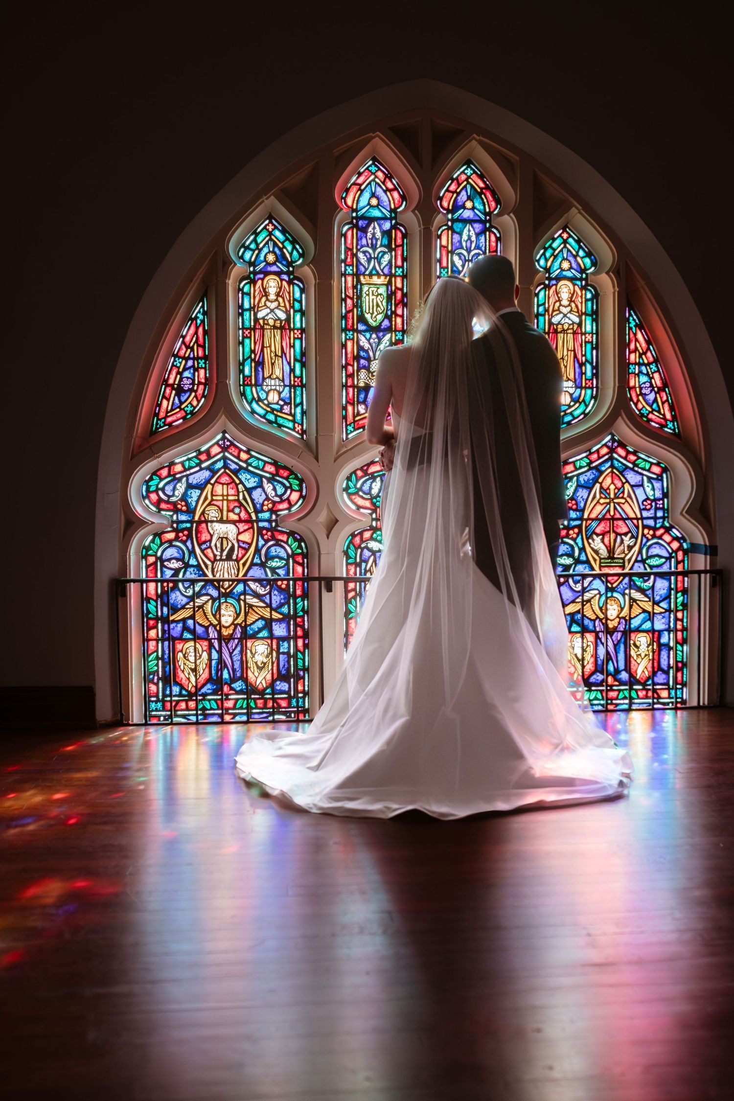 Bride and groom looking out of a stained glass window on their wedding day.