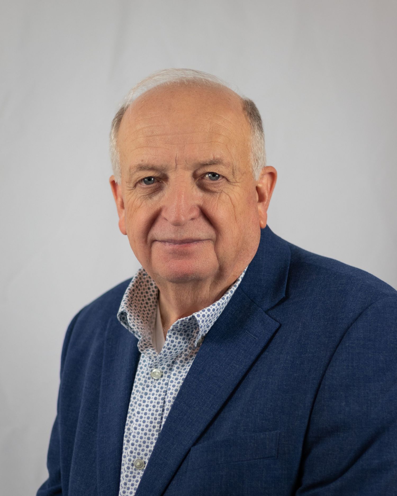 Senior man in a suit headshot against a white backdrop.