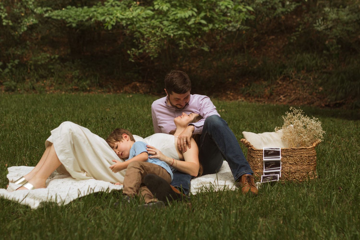 A family laying on the ground together with a basket that has ultrasound photos and flowers in it.