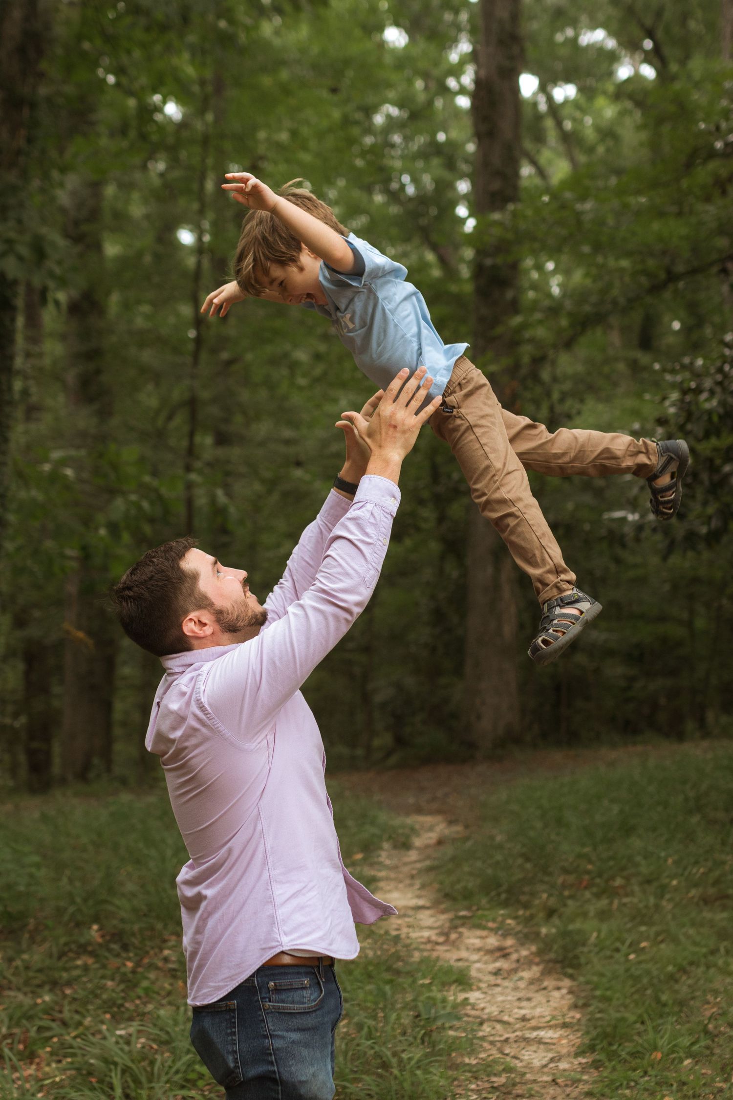 A dad in the woods throwing his young son in the air playfully.
