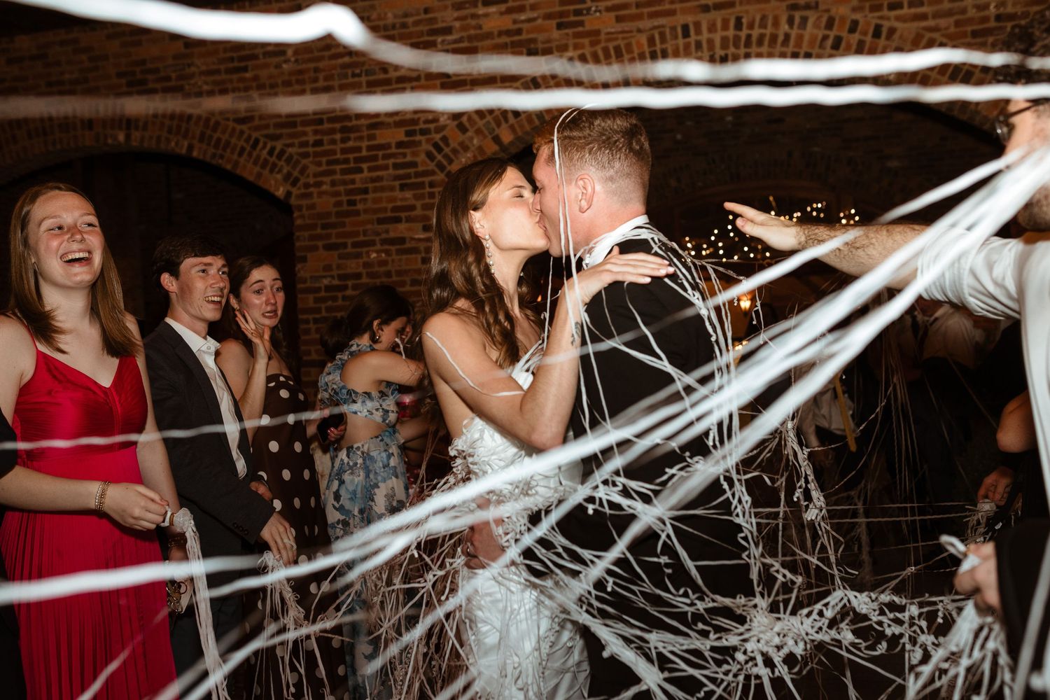 Bride and groom exit with streamers, kissing.