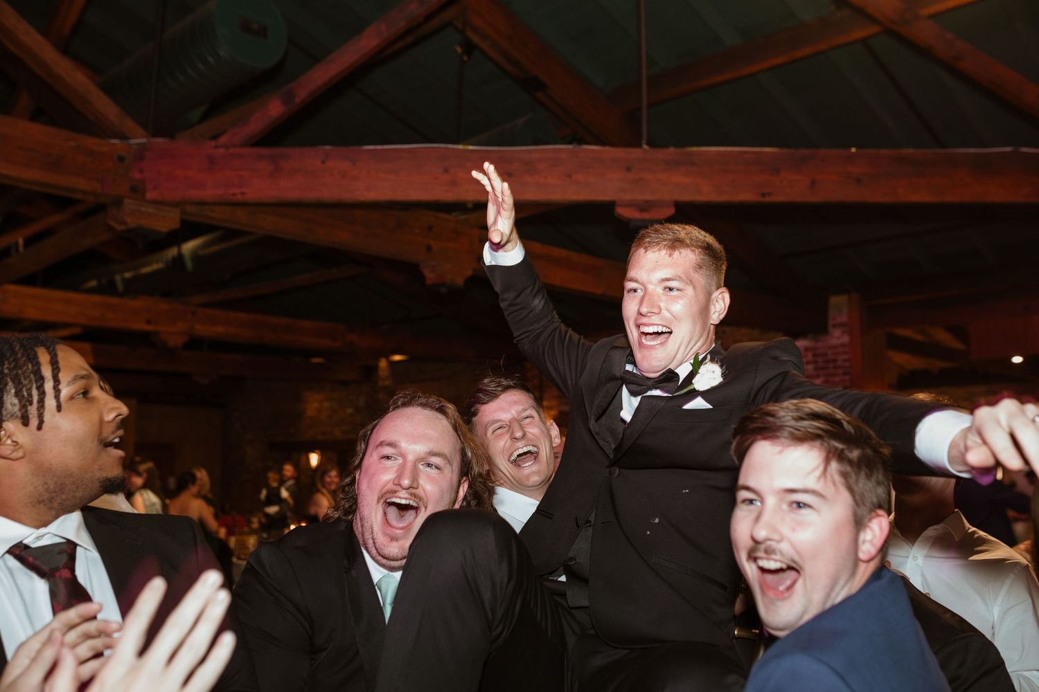Groom getting lifted in the air by his friends on his wedding day at the reception.